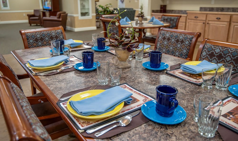 A neatly arranged dining table with blue cups, yellow plates, and napkins.