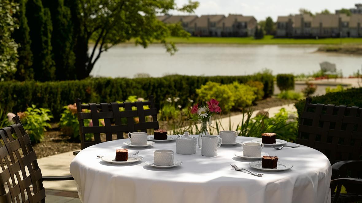 A beautifully set outdoor table overlooking a serene lake, with cups, saucers, and desserts ready for a delightful gathering.