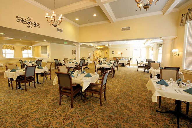 An elegant dining room setup with neatly arranged tables and chairs, adorned with chandeliers.