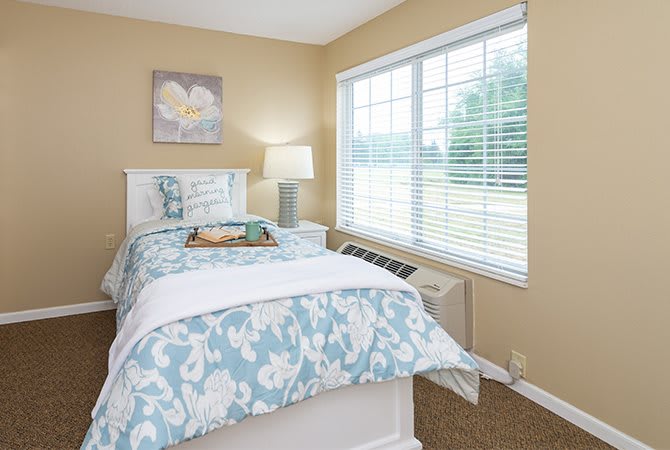 A cozy bedroom with floral bedding and a large window, allowing natural light to fill the space.