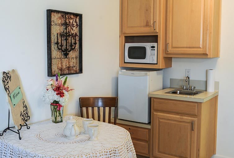 A small kitchen area with a microwave, sink, and a table adorned with flowers.