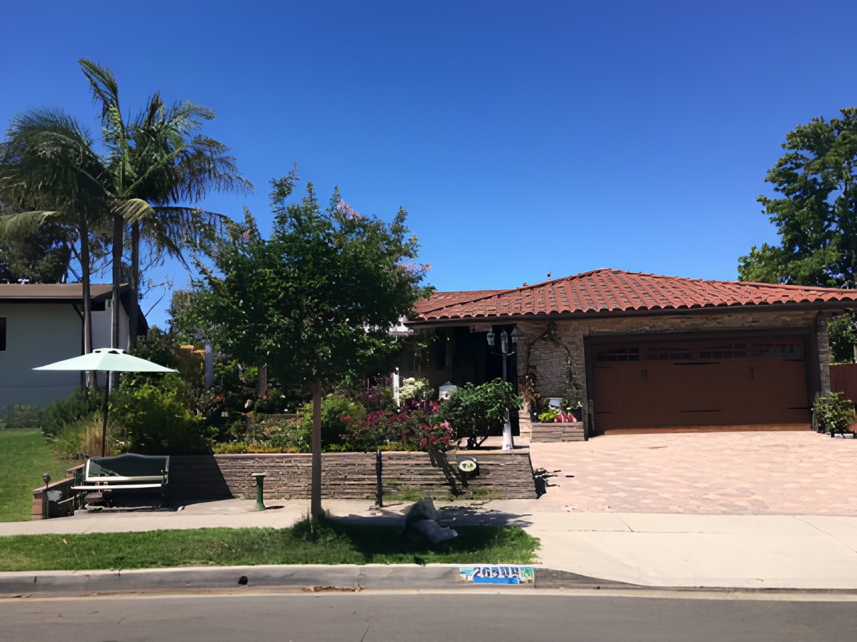 A suburban house with a landscaped yard and palm trees under a clear blue sky.