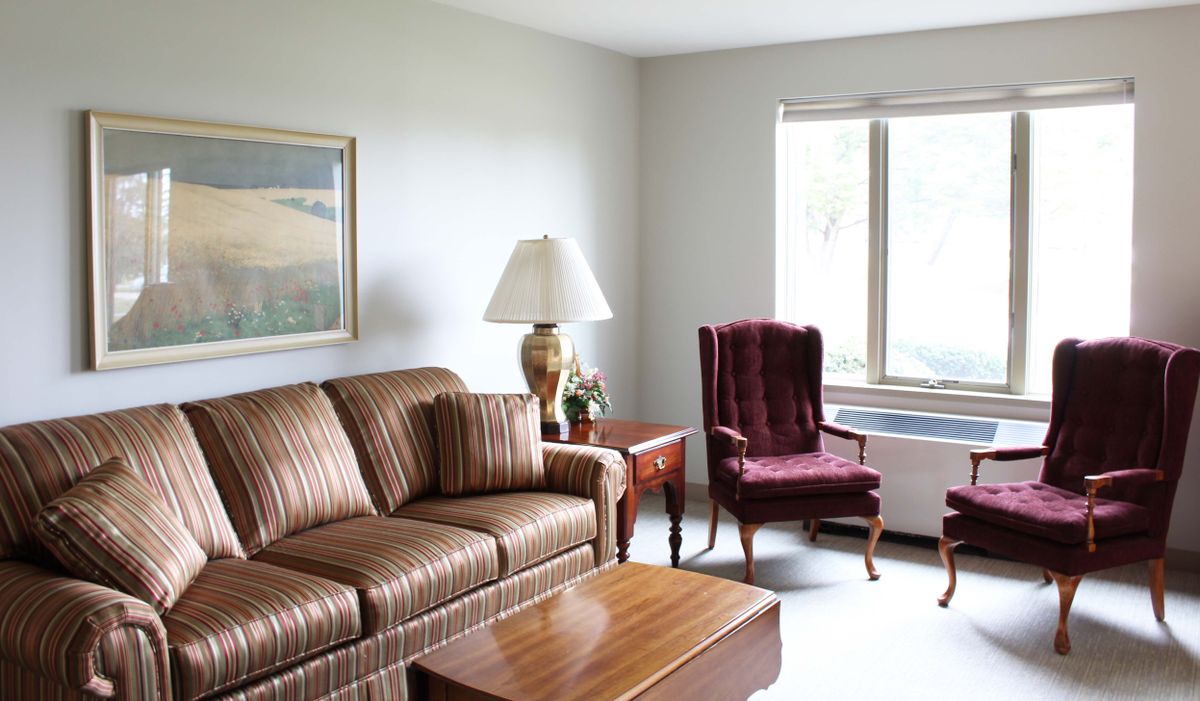 A cozy living room with a sofa, armchair, and coffee table, lit by natural light from the window.