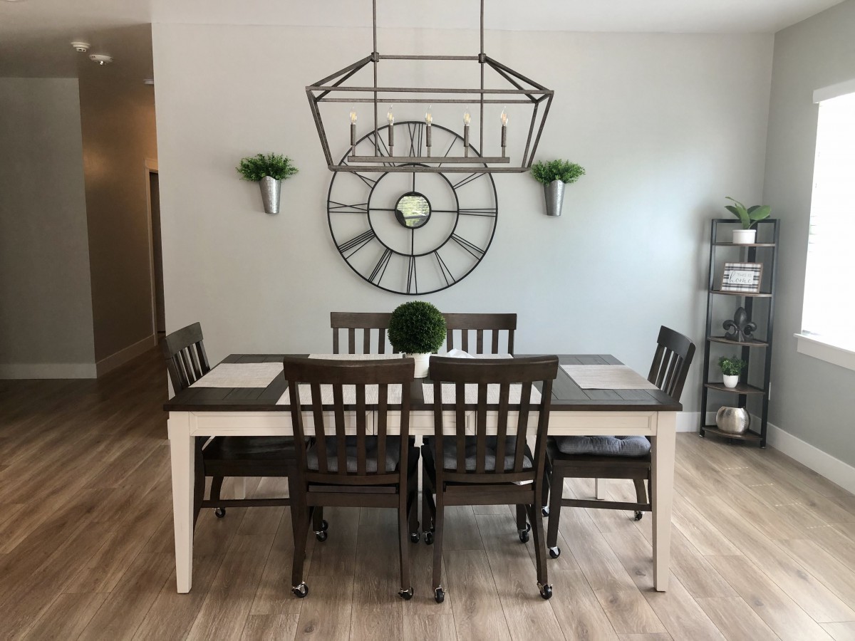 A modern dining room with a stylish dining set, geometric light fixture, and decorative wall clock.