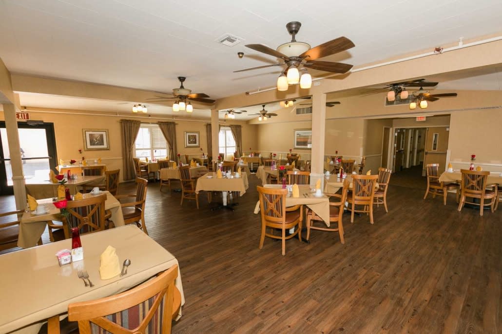 Spacious restaurant dining area with neatly arranged tables and chairs, featuring ceiling fans and a wooden floor.