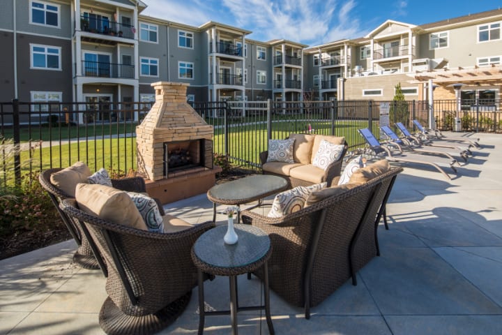 A cozy outdoor seating area with a fireplace in front of a modern apartment complex.