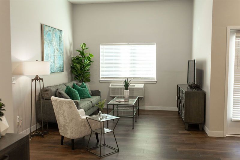A modern living room with a sofa, armchair, and coffee table, decorated with plants and artwork.