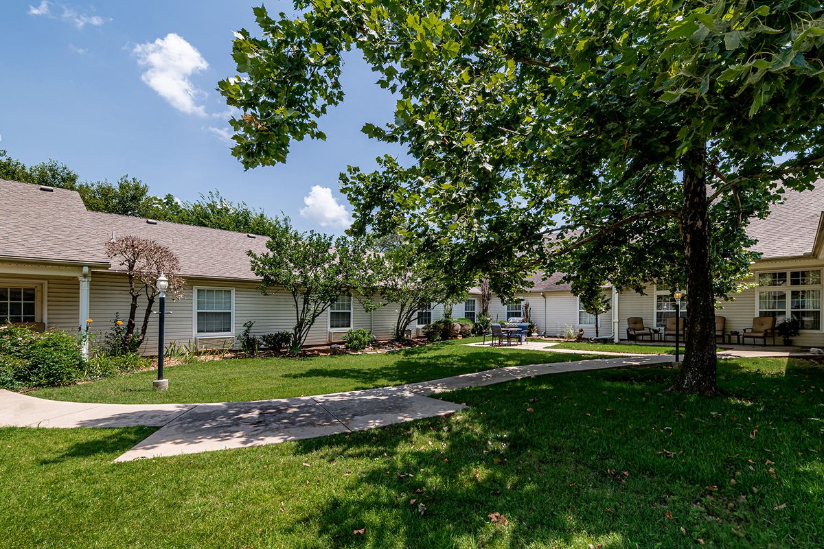 A suburban house with a lush green lawn and surrounding trees on a sunny day.