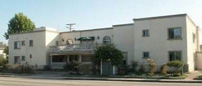 A street view of a residential building with a small porch and greenery in front.
