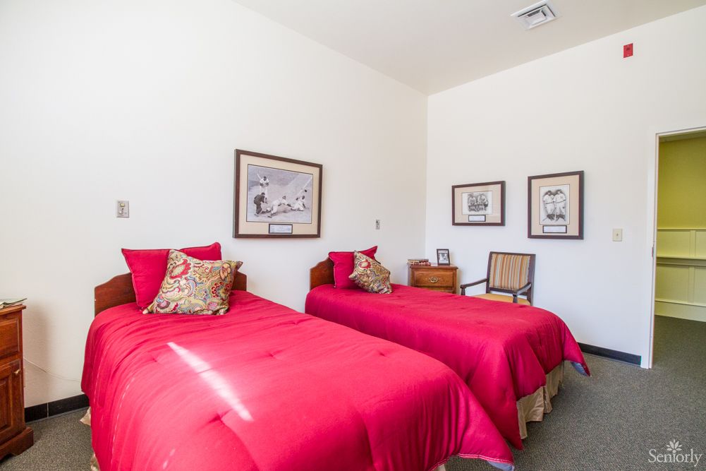 A neatly arranged bedroom featuring twin beds with vibrant red bedding and decorative pillows, complemented by framed artwork on the walls.