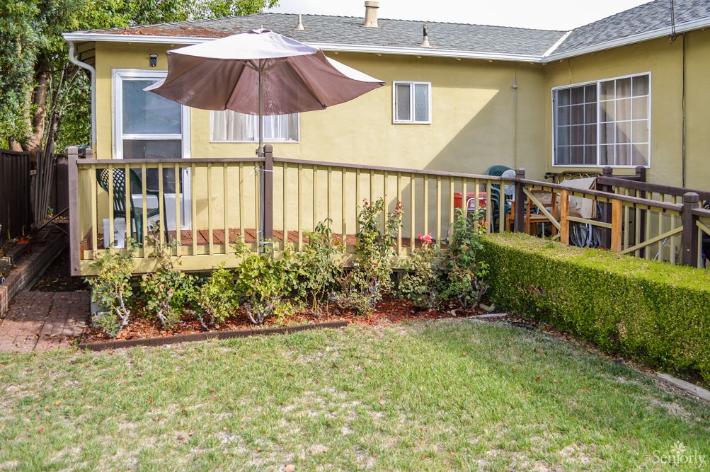 A backyard with a wooden deck, garden, and patio umbrella in front of a yellow house.