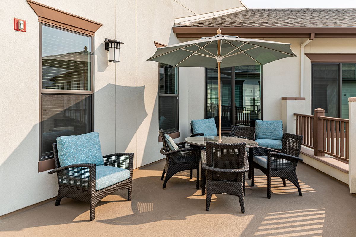 A modern outdoor patio with cushioned chairs, a table, and an umbrella.