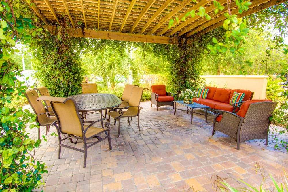A cozy patio area with comfortable outdoor furniture under a pergola surrounded by lush greenery.