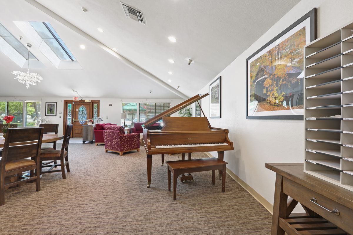 A spacious living room featuring a grand piano, comfortable seating, and artwork on the walls, illuminated by natural light from skylights.