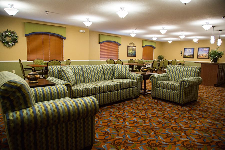 A spacious living room with green striped sofas and armchairs, featuring warm lighting and patterned carpet.