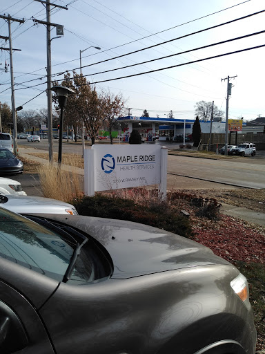 A view of a business sign from a parking lot, with cars parked in the foreground and a roadside setting.