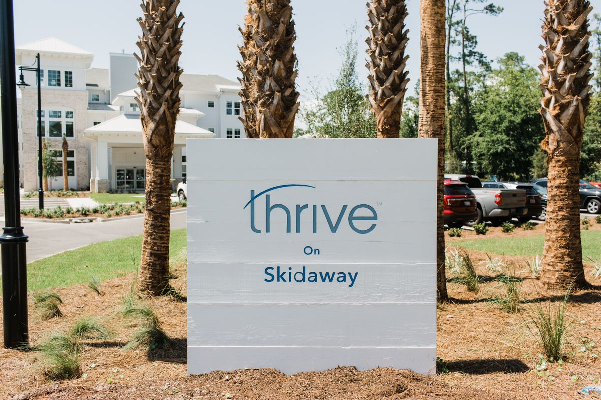A sign for Thrive on Skidaway, surrounded by palm trees and buildings.