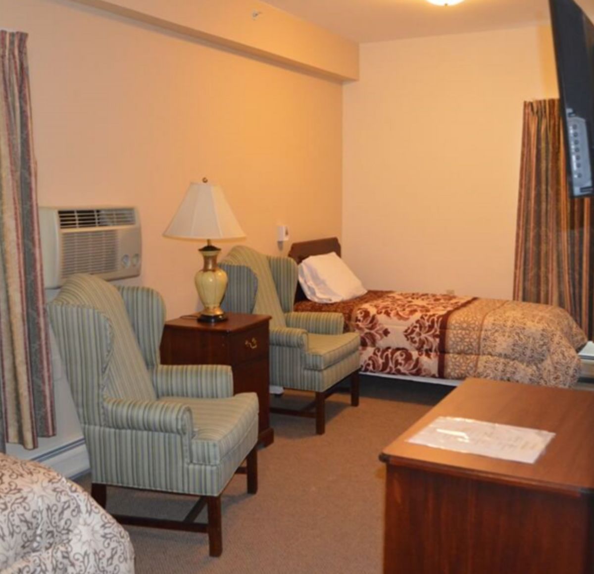 A cozy bedroom with two beds, two armchairs, a lamp on a nightstand, and a dresser.