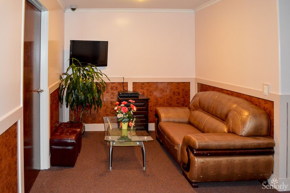 A cozy living room with a leather sofa, wall-mounted TV, indoor plant, and a glass table adorned with flowers.