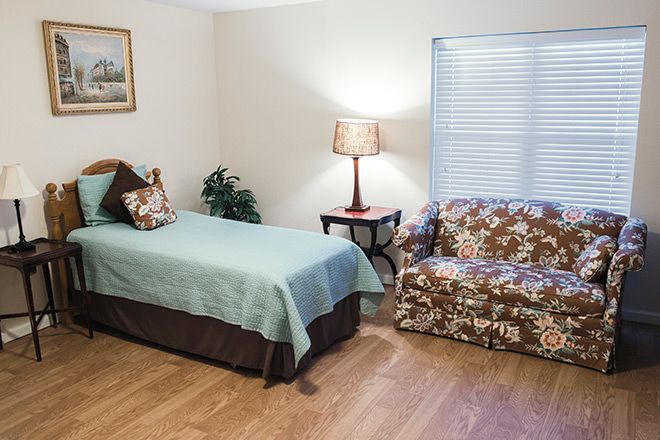 A cozy bedroom featuring a single bed with a turquoise cover, a floral-patterned couch, and a lamp on a side table.