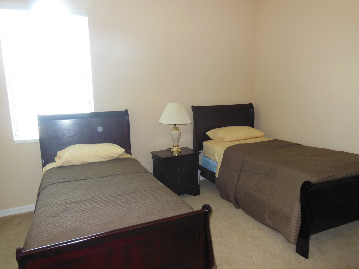 A simple bedroom with two twin beds and a nightstand with a lamp.