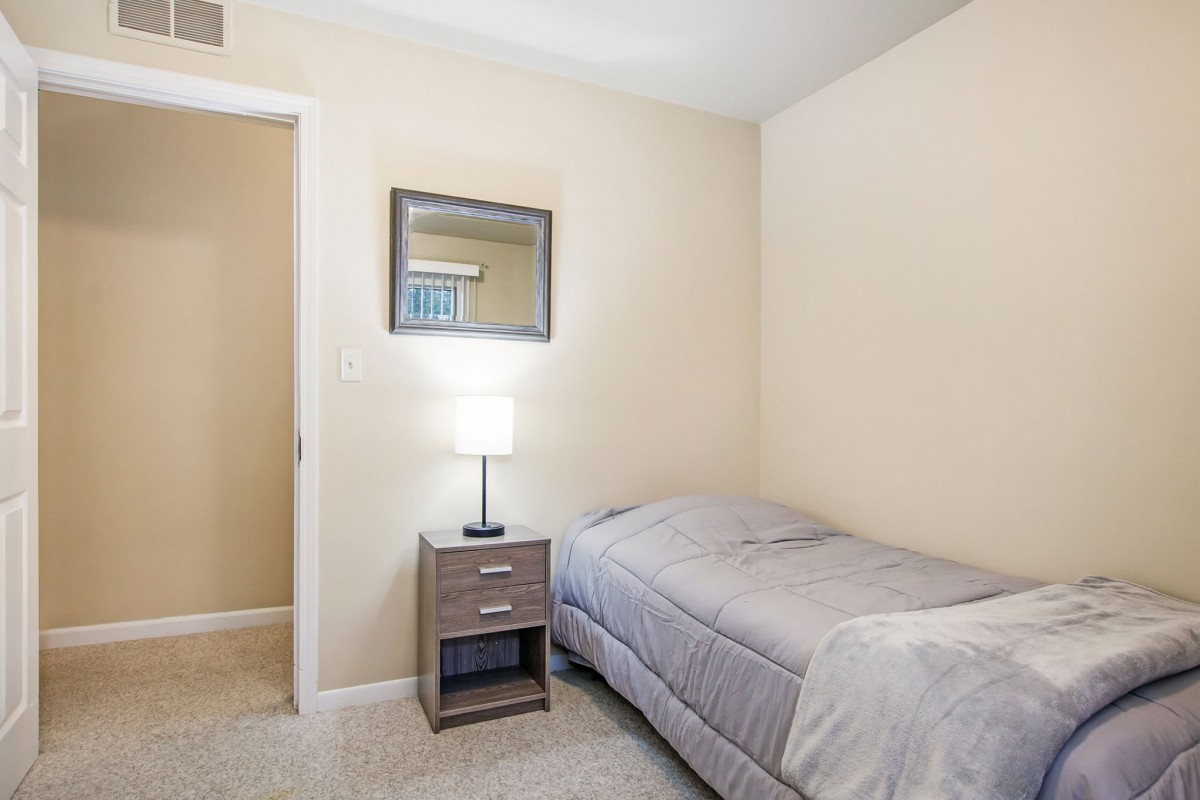 A minimalist bedroom with a single bed, nightstand, and lamp.