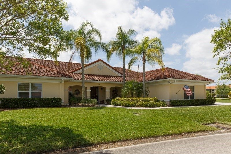 A suburban house with a tile roof and palm trees in the front yard, set against a clear blue sky.