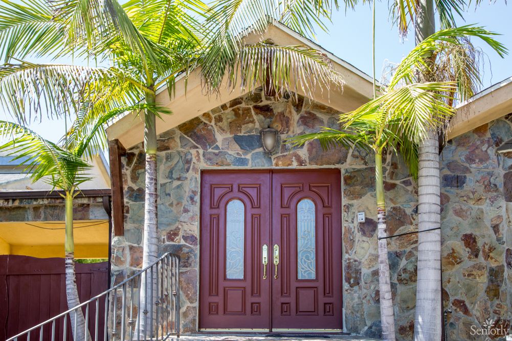 A stone building with large wooden double doors flanked by two palm trees.