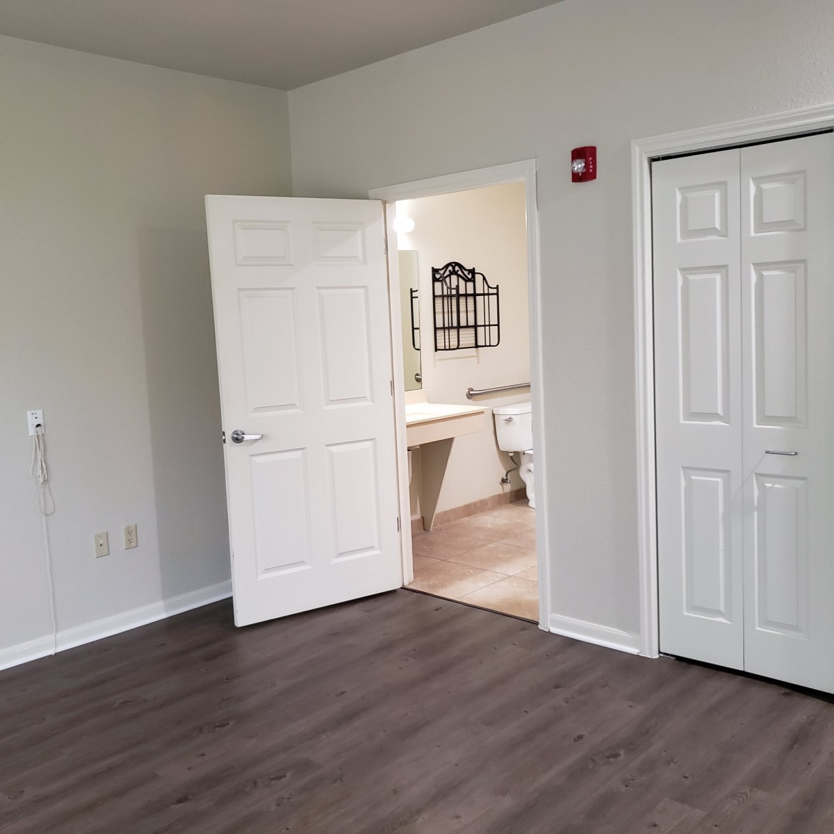 Empty room with a view into a bathroom, featuring hardwood floors and a closet.