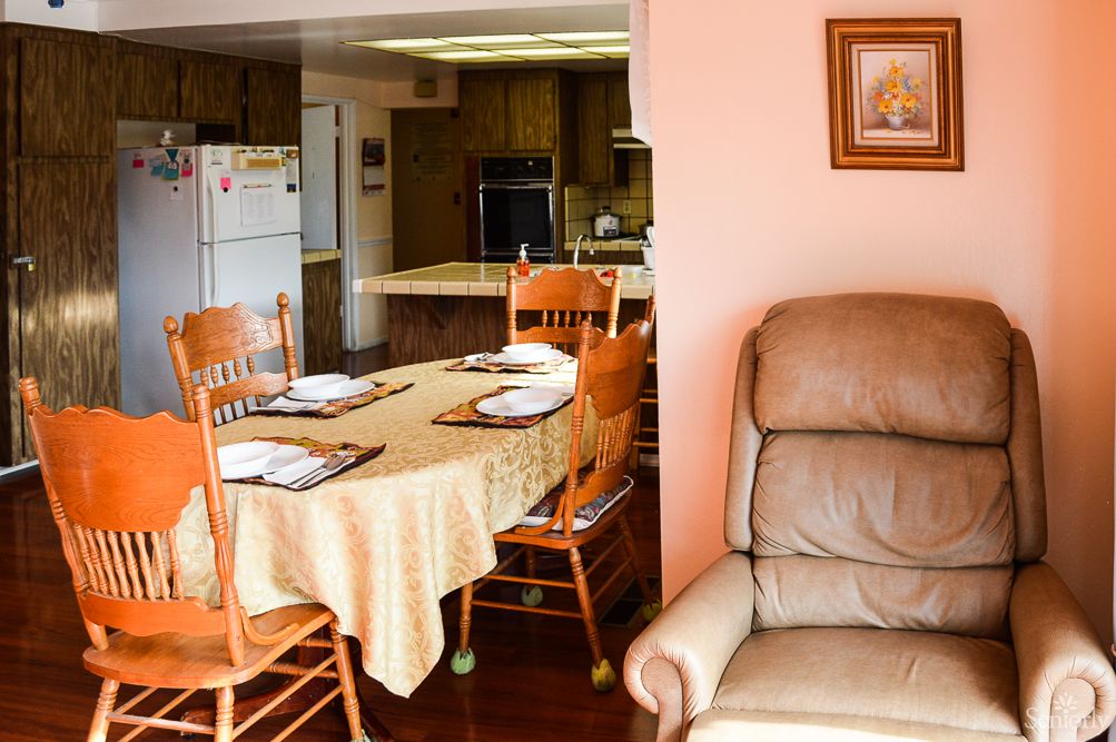 A cozy home interior featuring a dining area with a table set for four, adjacent to a kitchen and a comfortable recliner.