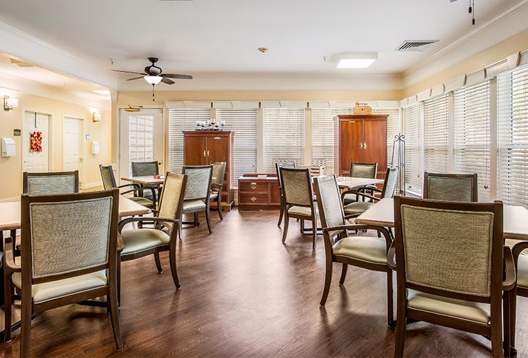 A spacious dining area with multiple tables and chairs, featuring a wooden floor and large windows.