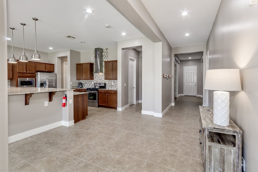 A modern kitchen and hallway area with tile flooring, wood cabinets, and recessed lighting.