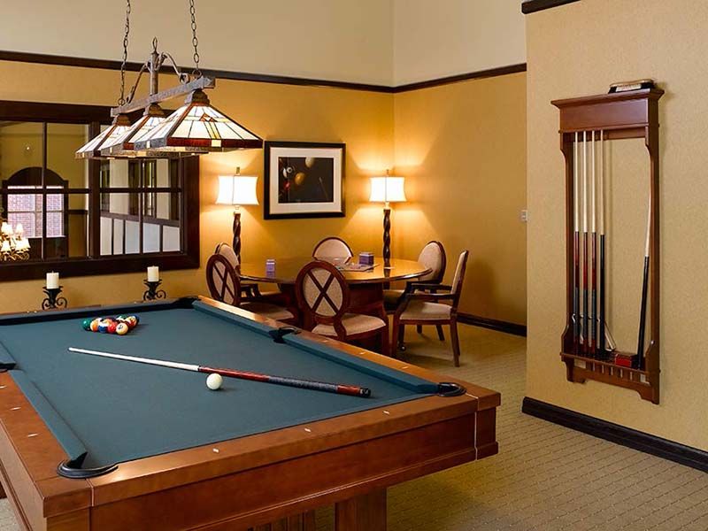 A cozy billiard room with a pool table and seating area, warmly lit by elegant lighting.