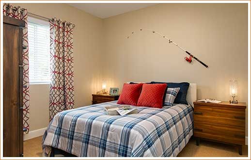 A cozy bedroom featuring a neatly made bed with plaid bedding and red accent pillows, illuminated by soft lighting from bedside lamps.