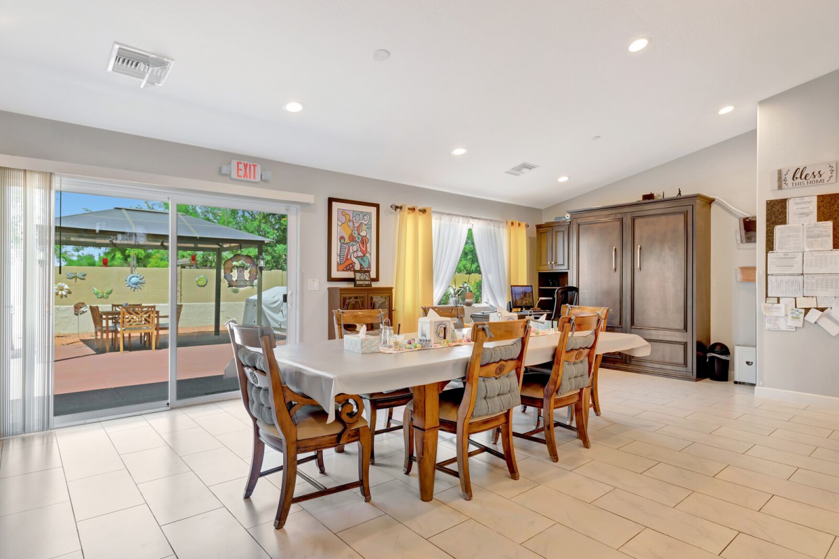A bright and spacious dining room with a large table and chairs, featuring a sliding glass door leading to the outdoors.