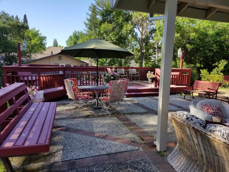 A spacious outdoor patio area with seating, tables, and an umbrella, surrounded by greenery.