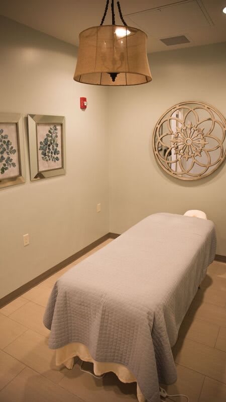 A peaceful massage room with a bed, wall decor, and gentle lighting.