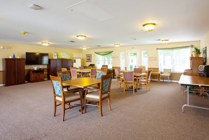 A spacious dining area with multiple tables and chairs, well-lit by natural light from large windows.