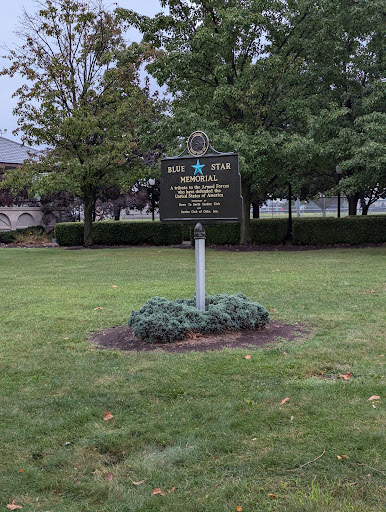 A historical marker stands in a green park, surrounded by trees.