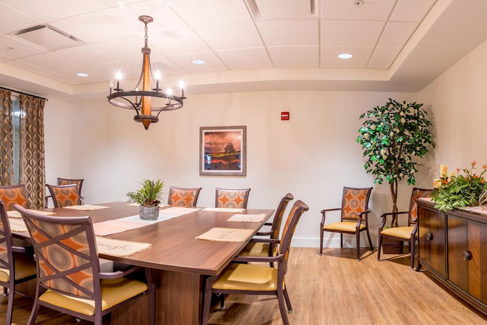 A well-furnished conference room with a large wooden table, cushioned chairs, a chandelier, and decorative plants.