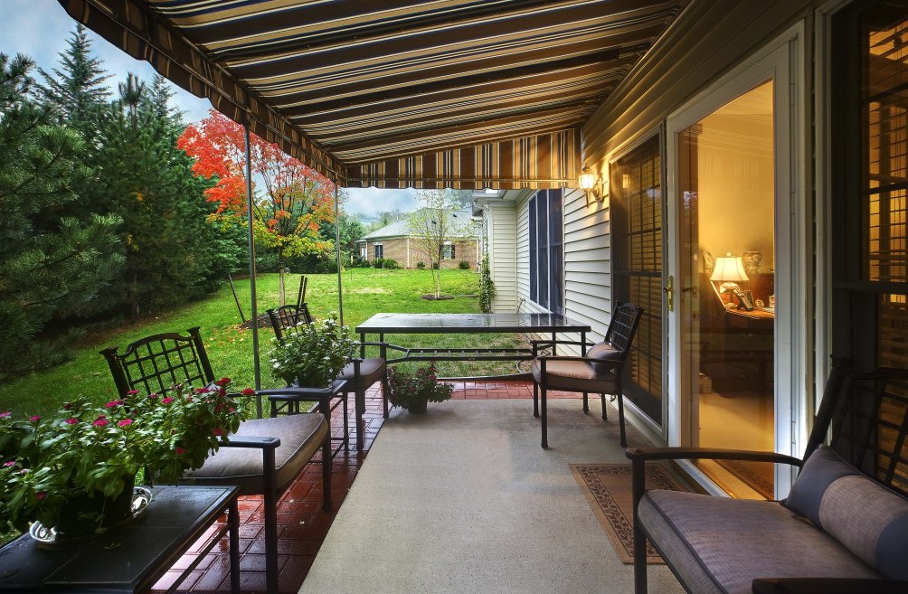 A cozy backyard patio with outdoor seating under a striped canopy, surrounded by a lush garden.