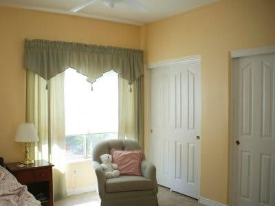 A cozy room featuring an armchair with cushions next to a window with curtains and a closet door.