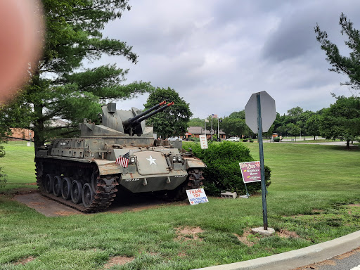 A military tank displayed in a grassy area near a stop sign.