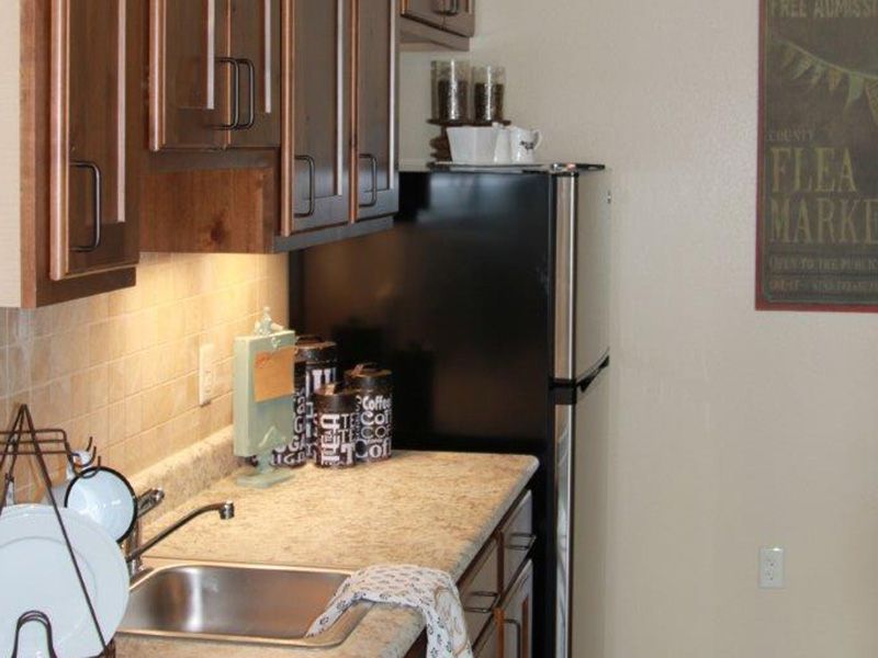 A compact kitchen with wooden cabinets, a countertop, and a black refrigerator.