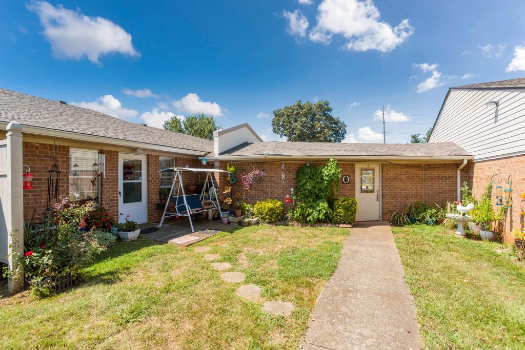 A cozy backyard with a swing set and a pathway leading to the house under a partly cloudy sky.