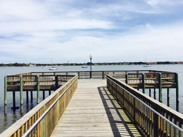 A wooden pier extending over calm water under a partly cloudy sky.