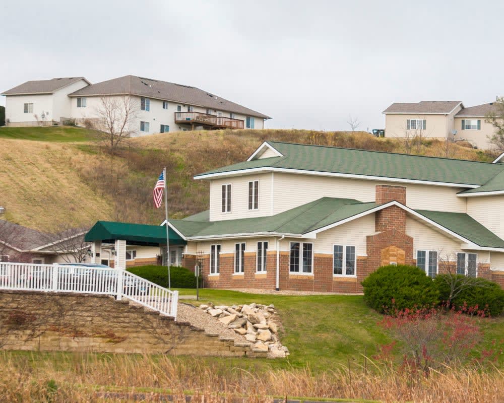 A suburban house with a green roof and a well-maintained yard, surrounded by other homes on a gentle hillside.