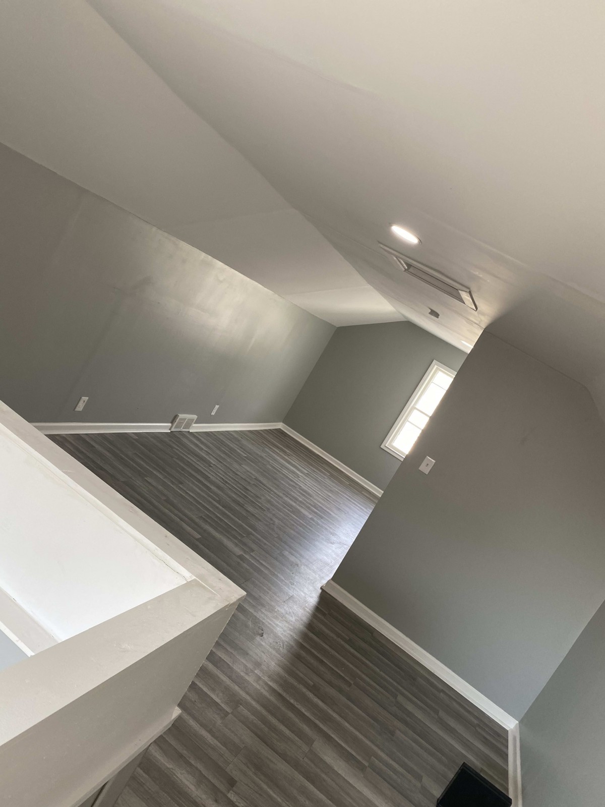 An empty room with gray walls and hardwood flooring, illuminated by natural light.