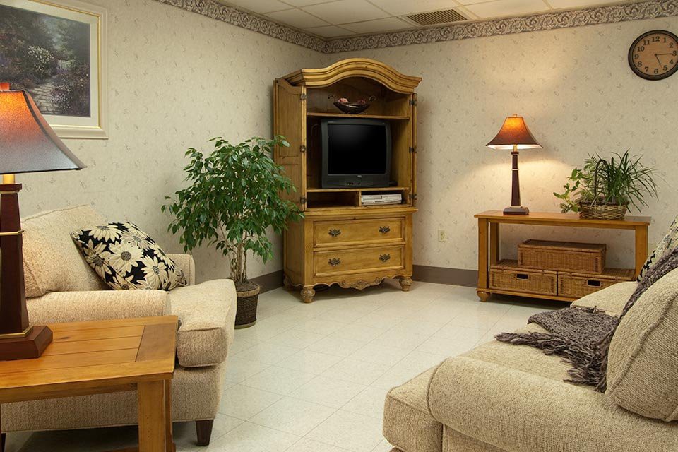 A cozy living room with a television on a wooden cabinet, surrounded by sofas and a lamp.