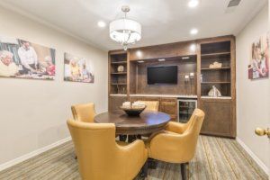 A modern dining room with yellow chairs and a round table, featuring built-in shelves and a television.